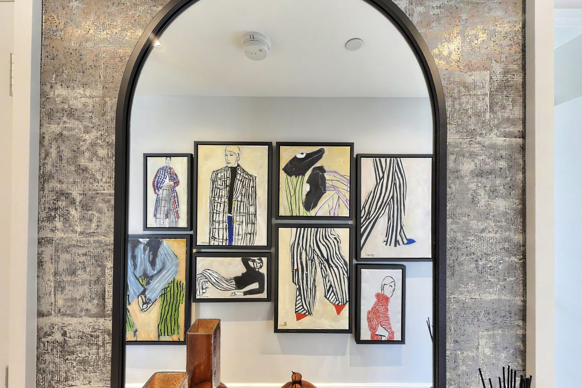 Arched mirror reflecting a gallery wall of fashion illustrations, framed by a textured metallic wall