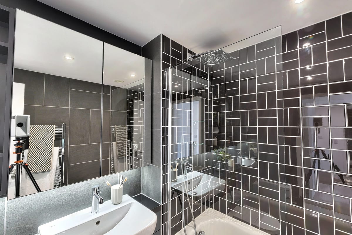 Bathroom with charcoal tiles laid in a herringbone pattern, glass shower screen and backlit mirror