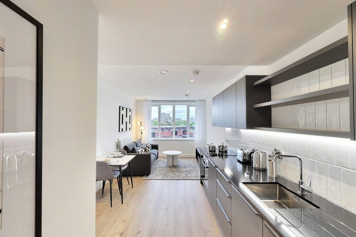 Galley kitchen with grey cabinetry and open shelving leading through to the living room and window