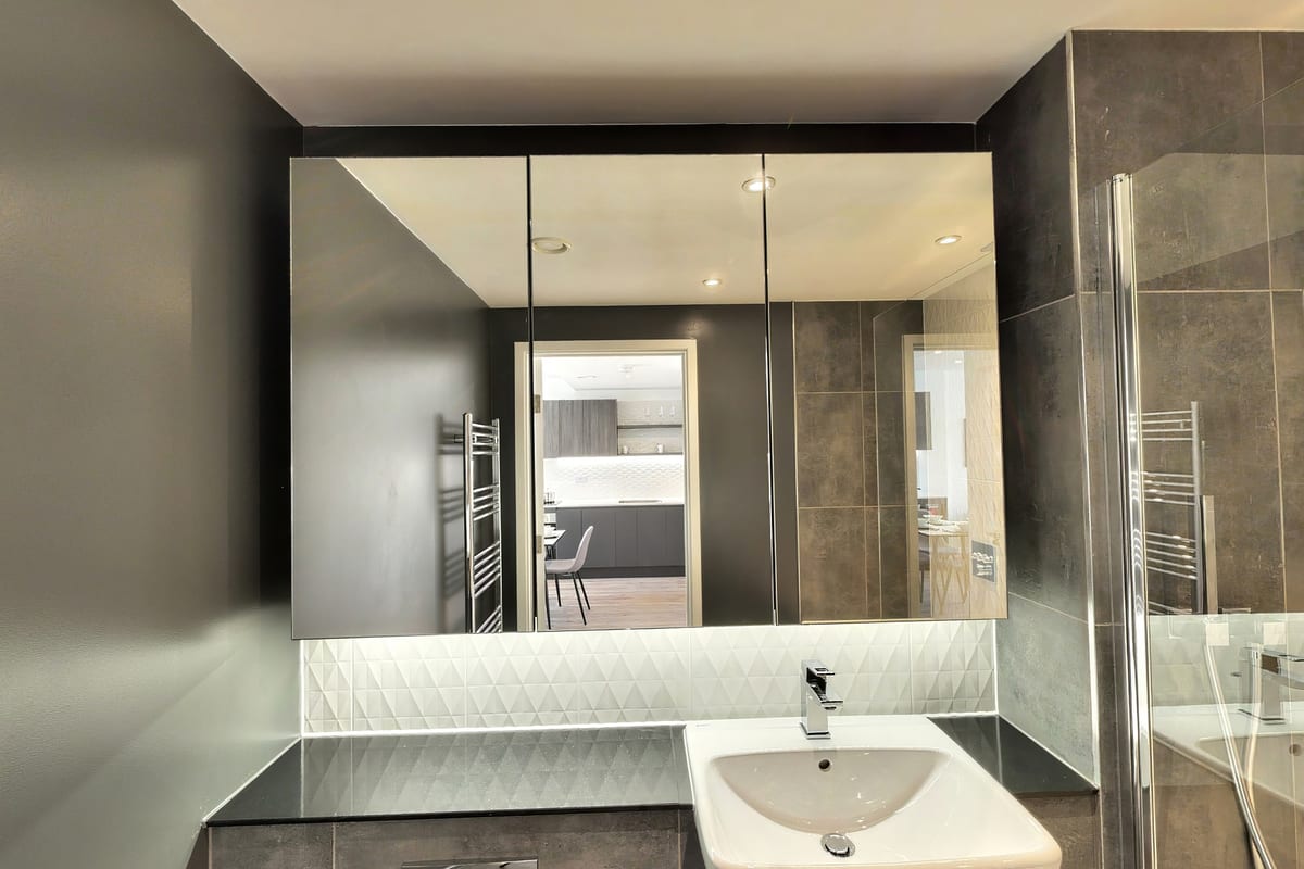 Bathroom with a charcoal tiled wall, mirrored cabinet with backlighting and a wall-hung basin