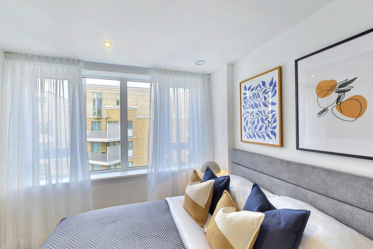 Bedroom with navy and mustard cushions, blue botanical prints and a sheer-curtained window