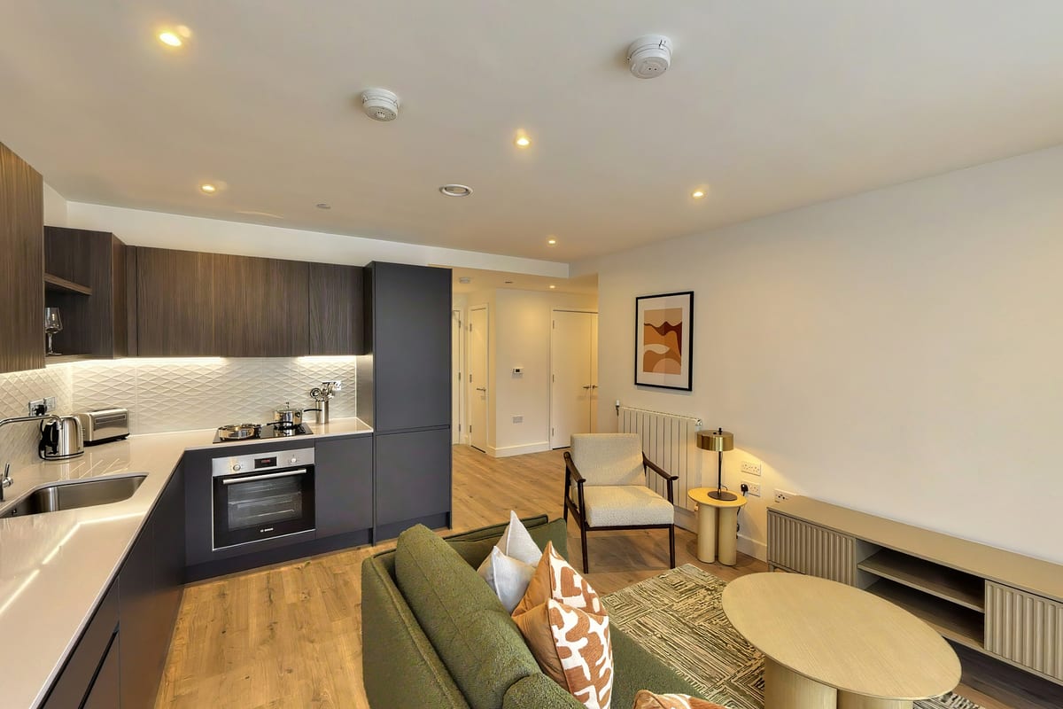 Open-plan living room looking towards the kitchen, with a green sofa, round coffee table and armchair