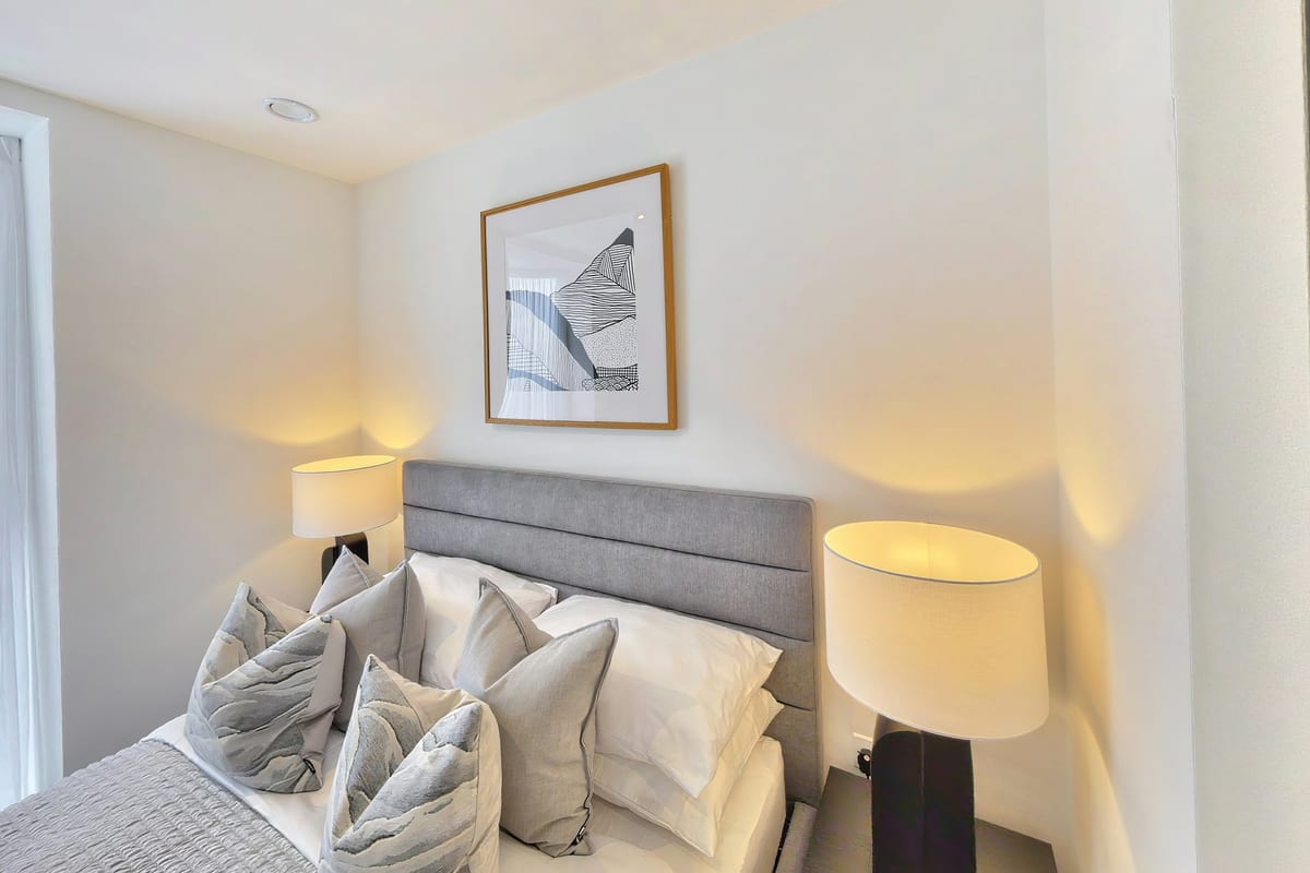 Bedroom with a grey upholstered headboard, bedside lamp and framed artwork