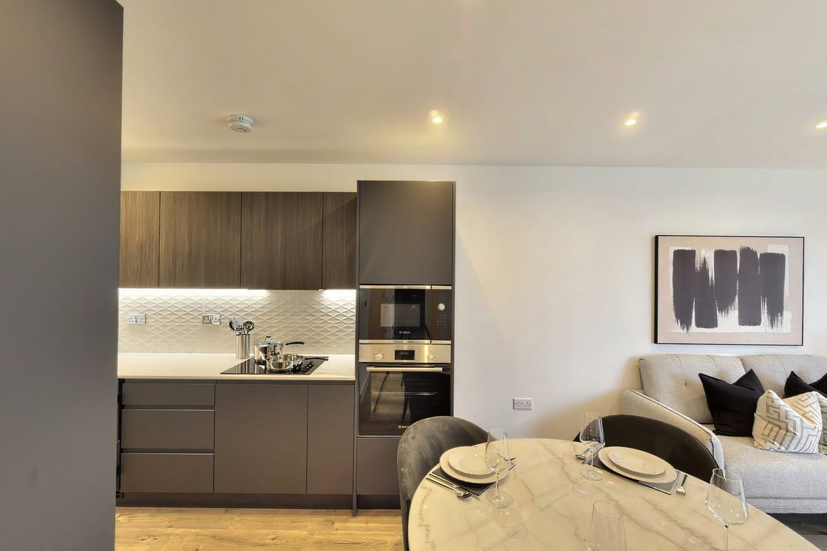 Round marble dining table in front of a walnut and charcoal fitted kitchen