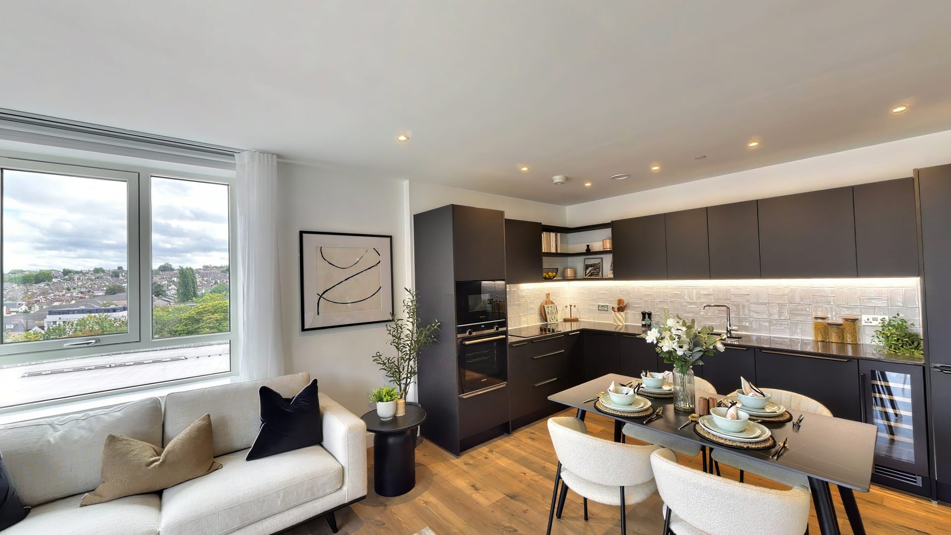 Living room in Myro House leading to a dark fitted kitchen and dining table, with tall windows over the rooftops